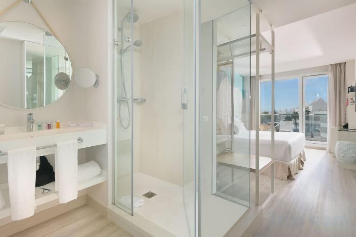 Ein modernes Hotelzimmer mit Duschkabine aus Glas, einem großen Bett und Blick auf die Stadt.
