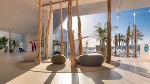 A modern lobby with a view of the beach, featuring wooden pillars, seating areas, and potted plants. - Amàre Beach Hotel Ibiza - Adults Recommended (Sant Josep de sa Talaia)