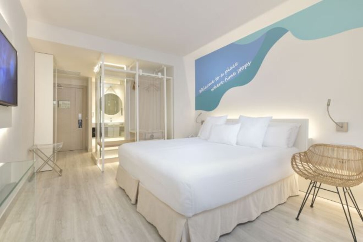 Quarto de hotel com cama grande, área de estar e televisão na parede.
