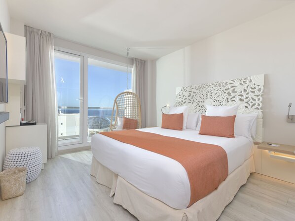 A modern hotel room with a large bed, a hanging chair, and a view of the sea.