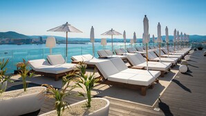 A sunlit deck with rows of white lounge chairs and umbrellas, overlooking a calm sea and distant cityscape. - Amàre Beach Hotel Ibiza - Adults Recommended (Sant Josep de sa Talaia)