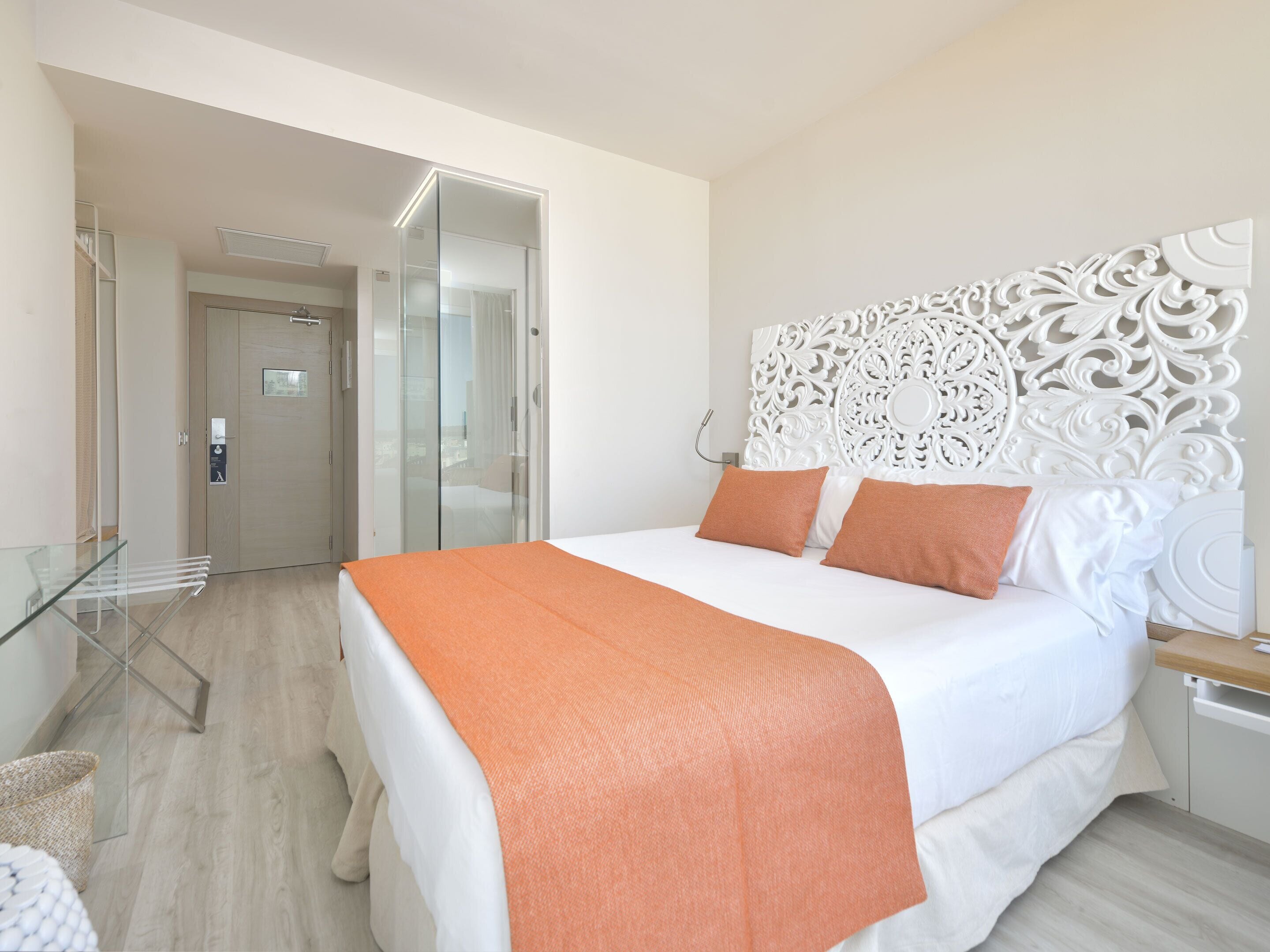 A modern hotel room with a large bed, a glass partition wall, and a decorative headboard.