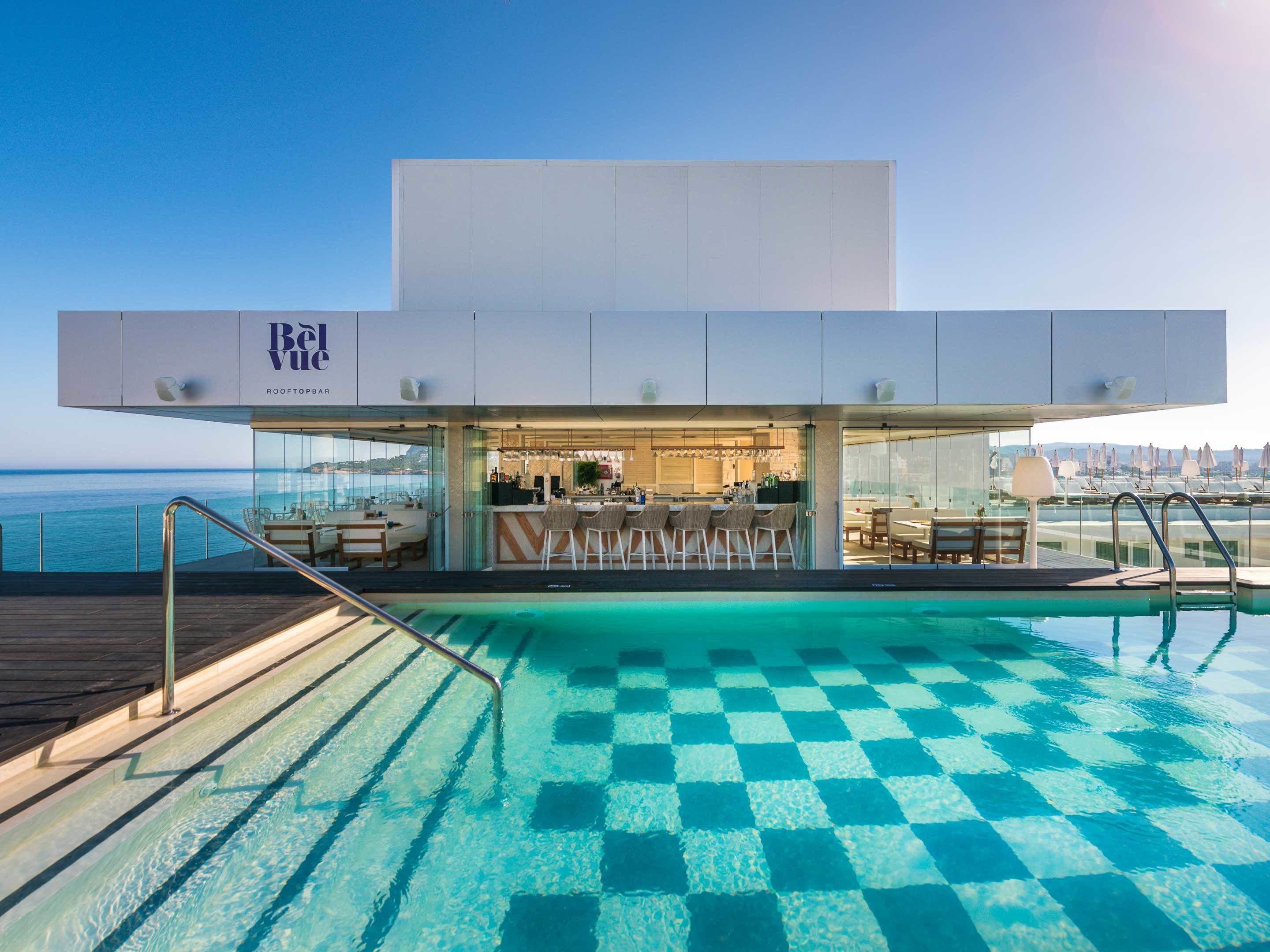 Un bar en la azotea con piscina, taburetes y vistas al océano.