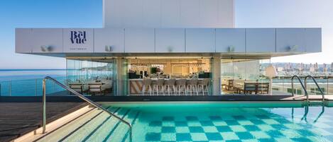 Un bar en la azotea con piscina, taburetes y vistas al océano.