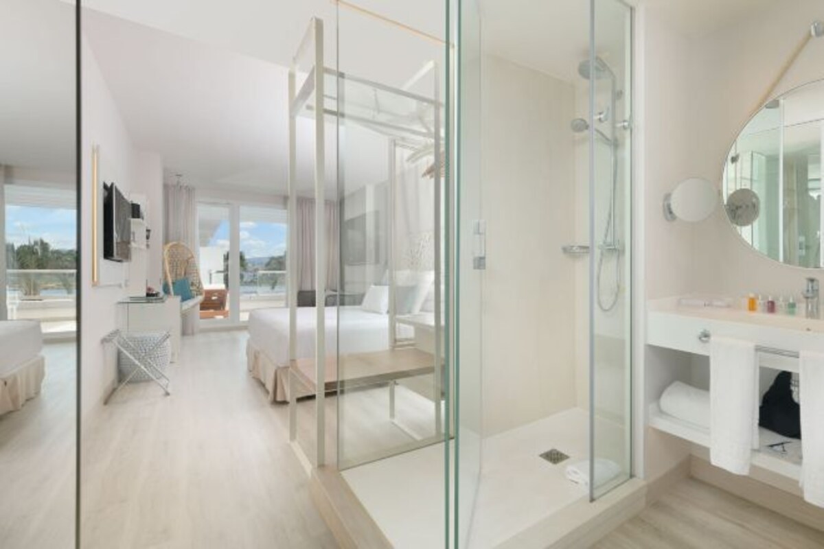 Quarto de hotel moderno com chuveiro em vidro, varanda e vista para a cidade.