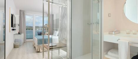 Una habitación de hotel moderna con cabina de ducha de vidrio, cama con vista al mar, balcón y un espejo grande.