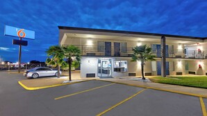 Un motel con un letrero grande, un estacionamiento y un edificio con varias puertas y ventanas.
