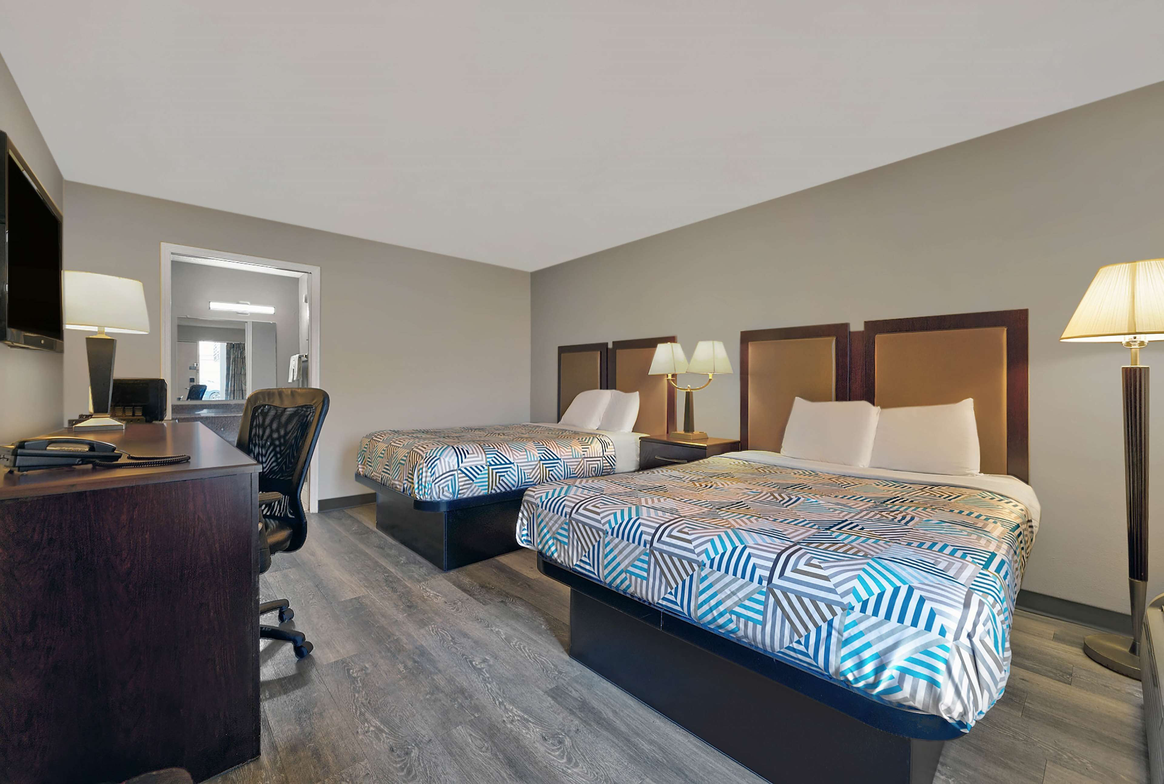 A hotel room with two beds, a desk, a chair, and a TV.