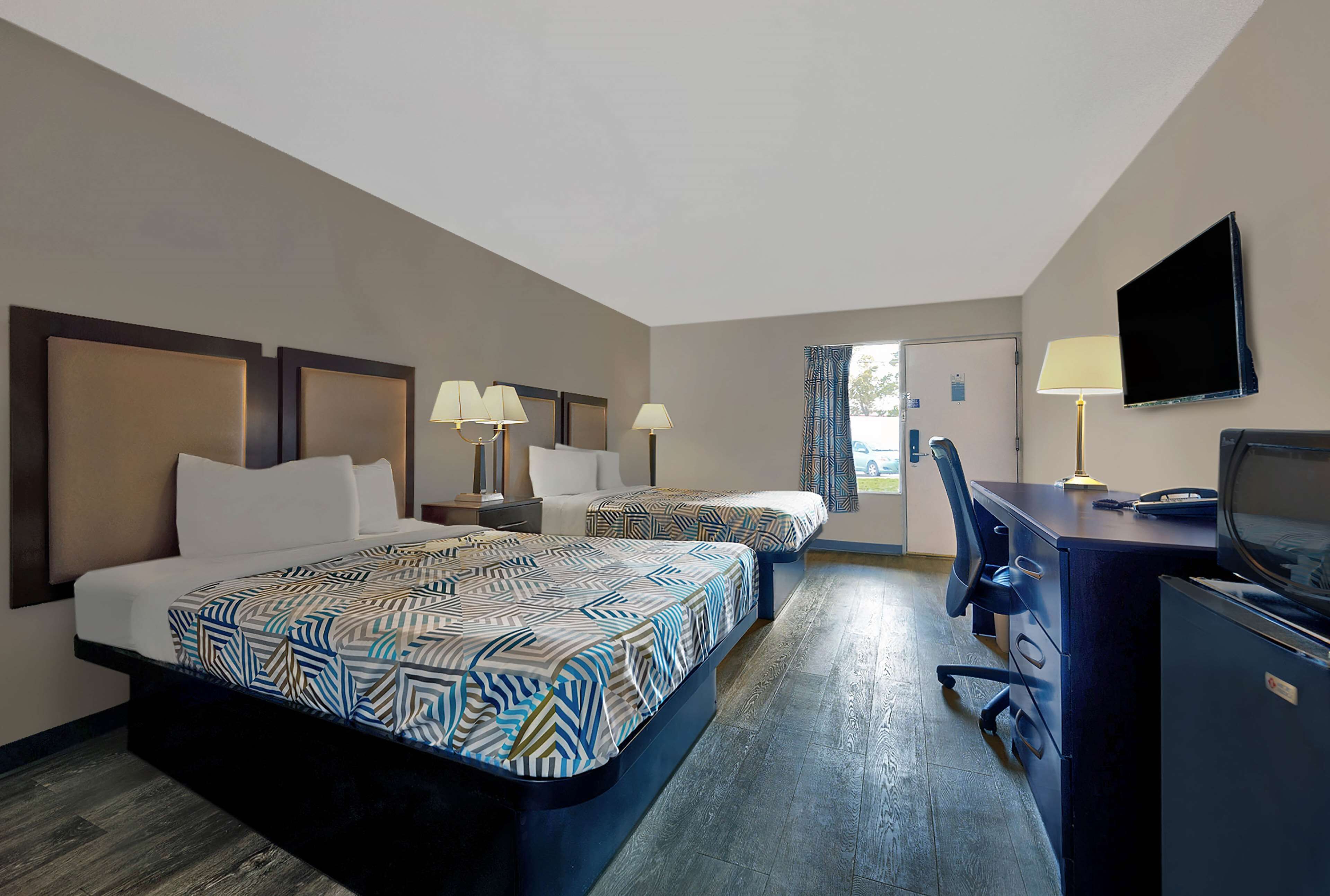 A hotel room with two beds, a desk, a chair, a TV, and a window with curtains.