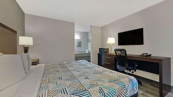 A hotel room with a bed, a desk, a chair, a television, and a bathroom in the background.