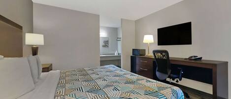 A hotel room with a bed, a desk, a chair, a television, and a bathroom in the background.