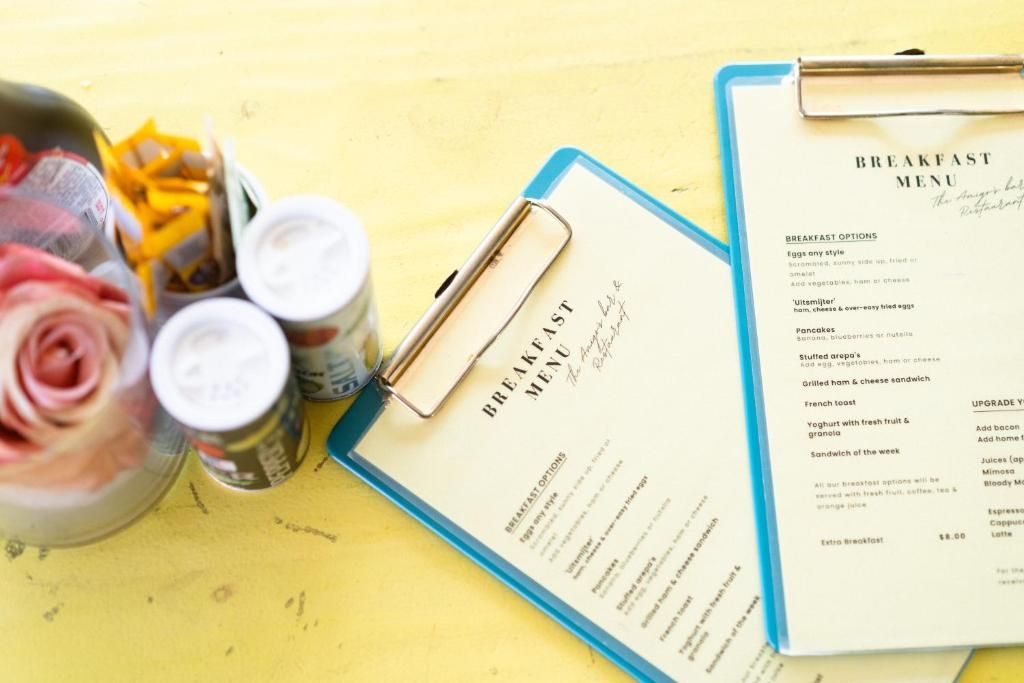 Een ontbijtmenu op een klembord, met een pen, een pot jam en een pot augurken op een gele ondergrond.