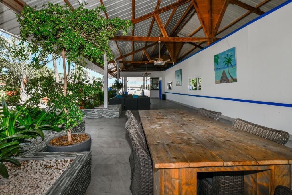 A covered outdoor area with a wooden table and benches, surrounded by potted plants and a view of the sea.