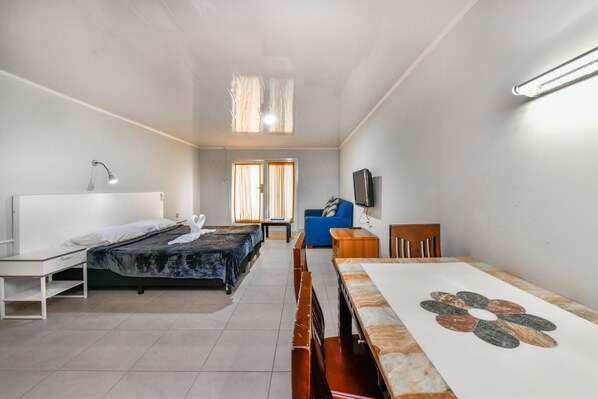 A room with two beds, a desk, a chair, a TV, and a window with curtains. - Aruba Blue Village (Noord)