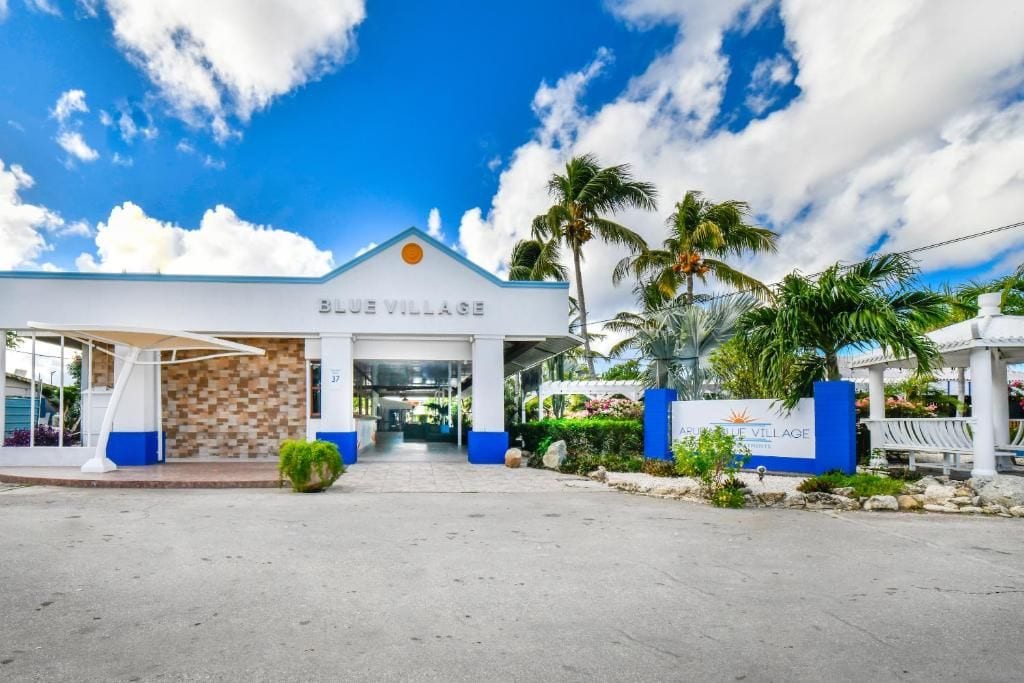 L’entrée d’un hôtel, avec une enseigne indiquant « BLUE VILLAGE » et une allée couverte.
