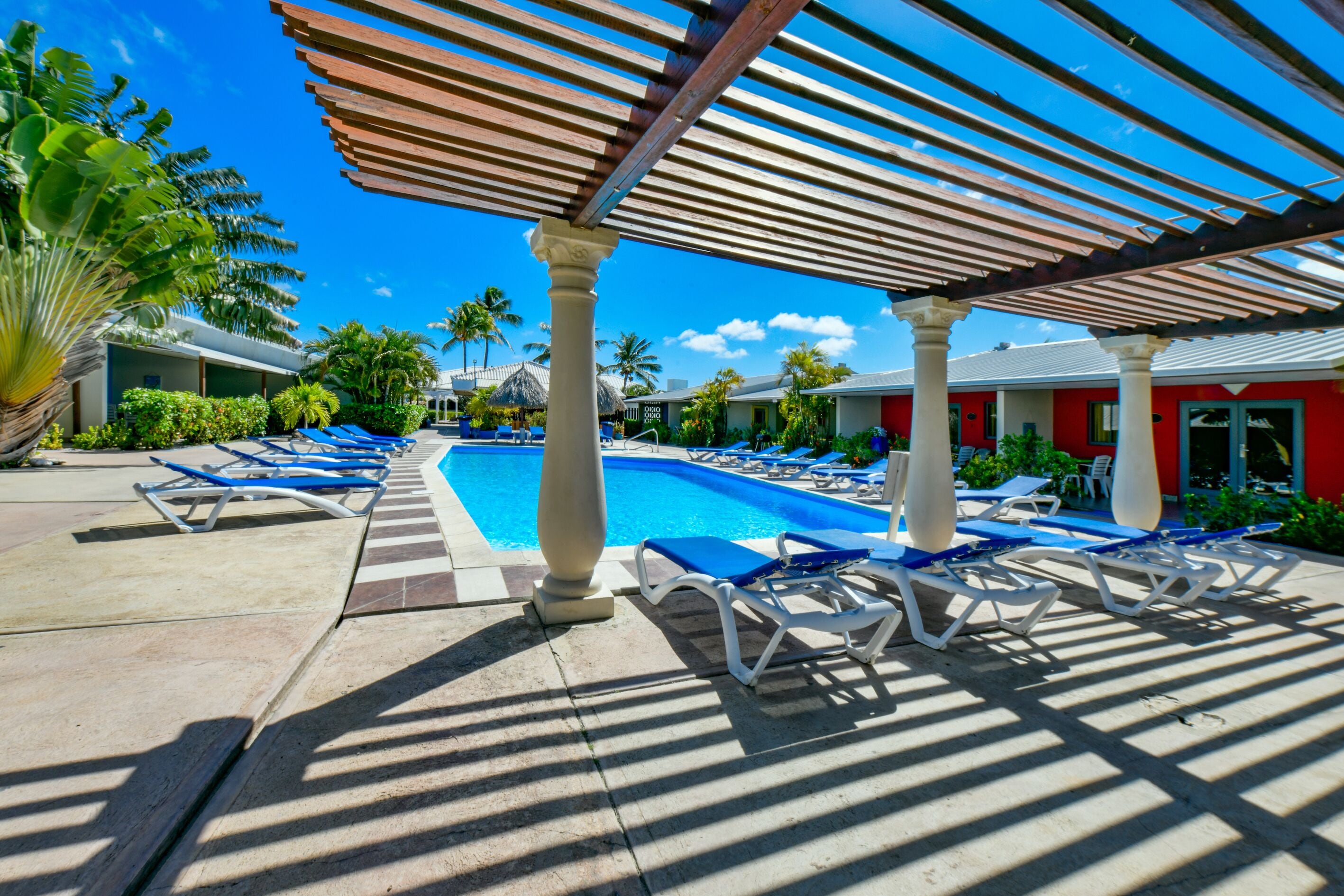 Zona junto a la piscina con sillones de descanso, piscina y un área de estar cubierta.