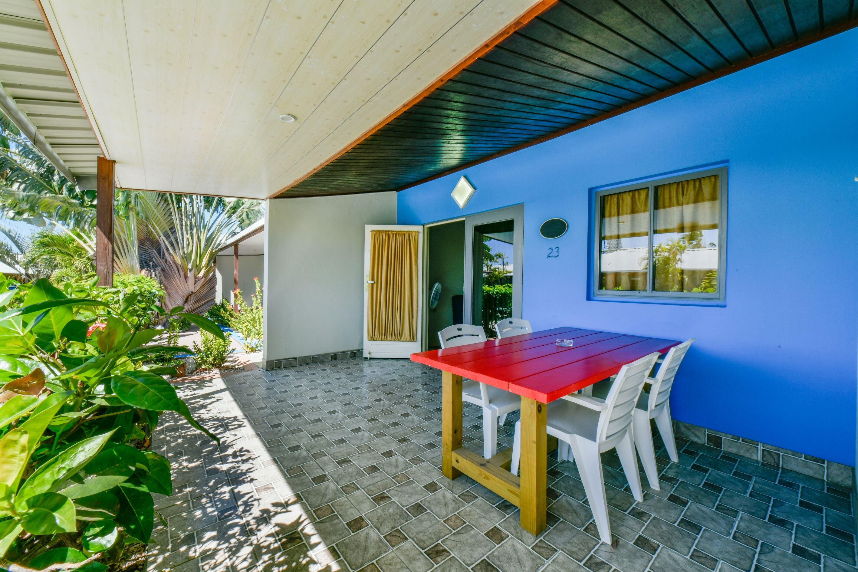 A covered patio area with a red table and white chairs, a blue wall, and a tiled floor.