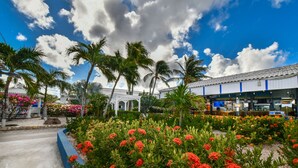 Hotel met een tuin vol rode bloemen, palmbomen en een wit gebouw met pannendak.