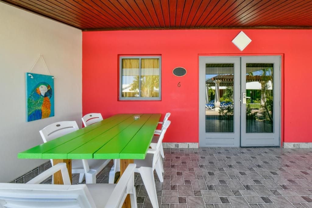 A room with a green table and white chairs, a red wall, a window with curtains, and a door with glass panels.