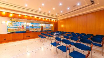 A conference room with rows of blue chairs, a wooden panel wall, and a large window with artwork.