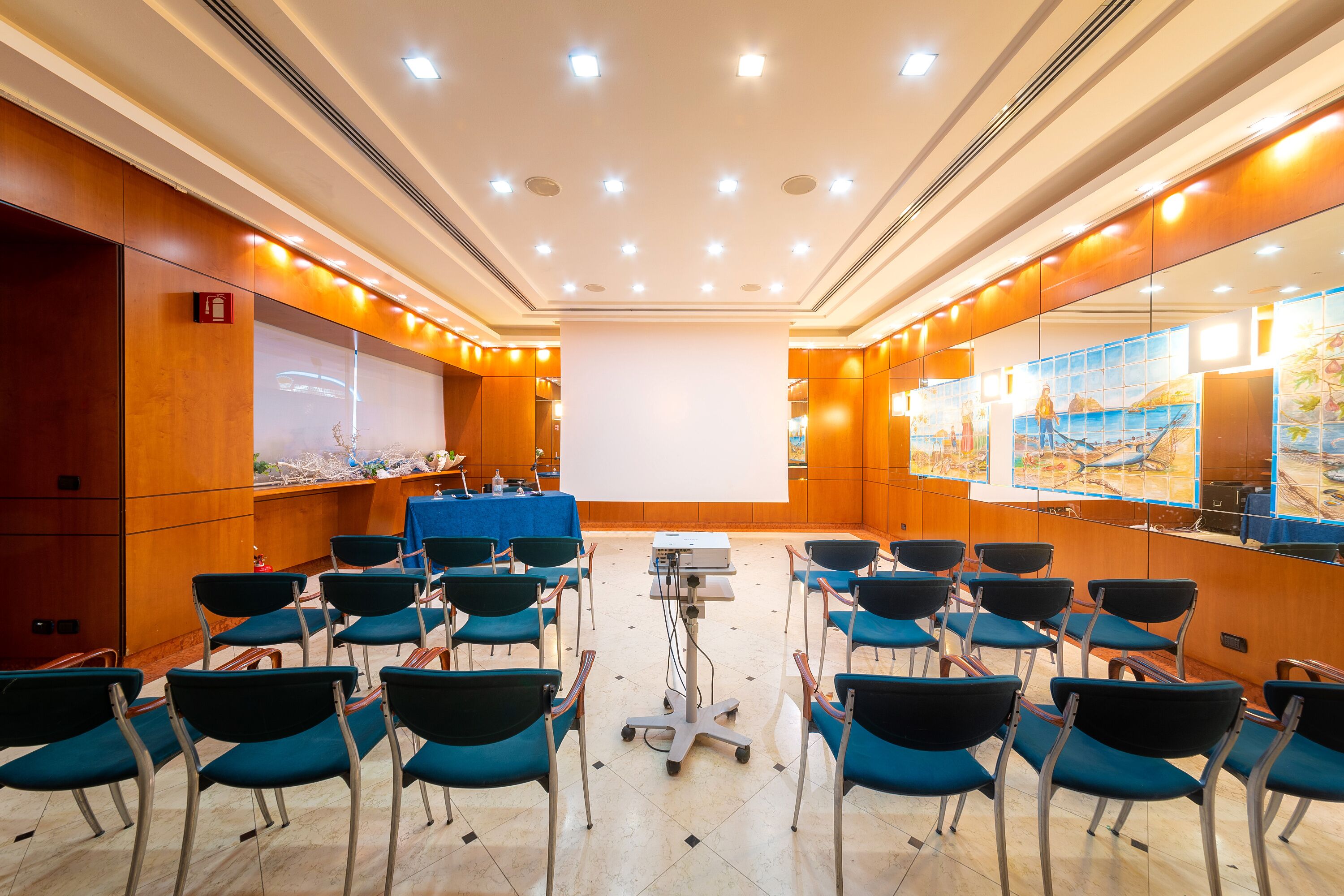 A conference room with rows of chairs, a projector, and a large screen.