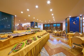 A buffet setup with various food items, a decorative sailboat, and a room with tables and chairs. - Grand Hotel Delle Terme Re Ferdinando (Ischia)