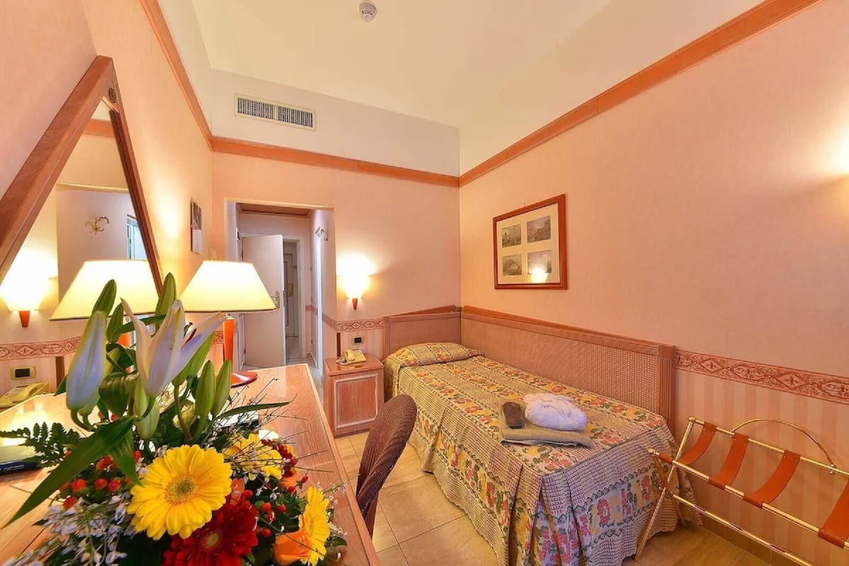 Una camera d'albergo con un letto, un comodino, una lampada e uno specchio.