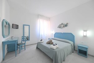 Quarto com cama, escrivaninha, cadeira, televisão e mesa de cabeceira.