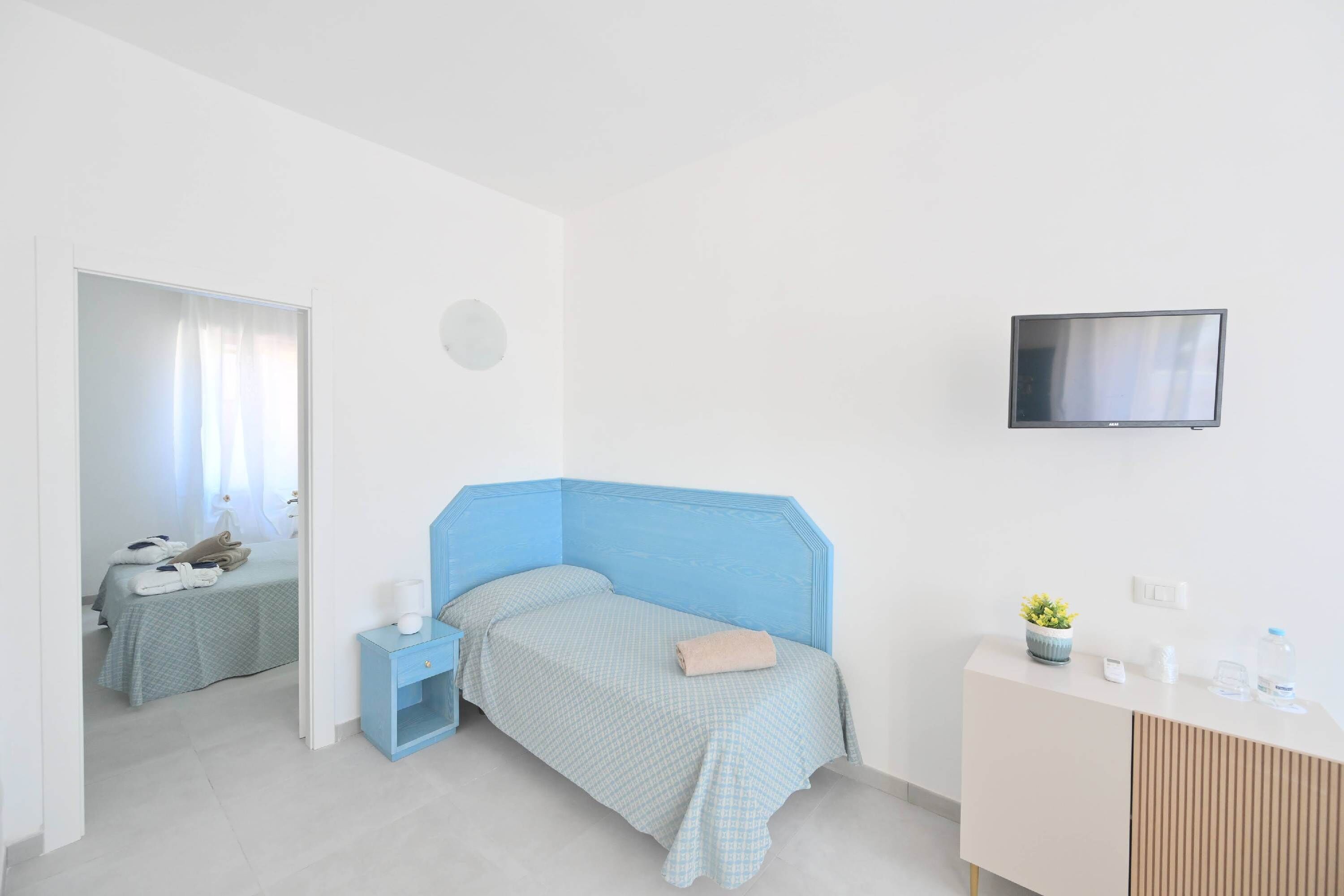A bedroom with a bed, a nightstand, a dresser, a television, and a bathroom visible through an open door.