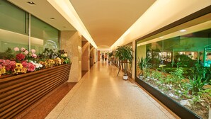 Un pasillo con un banco de madera decorado con flores, un muro de cristal con vistas a un jardín y un piso de baldosas.