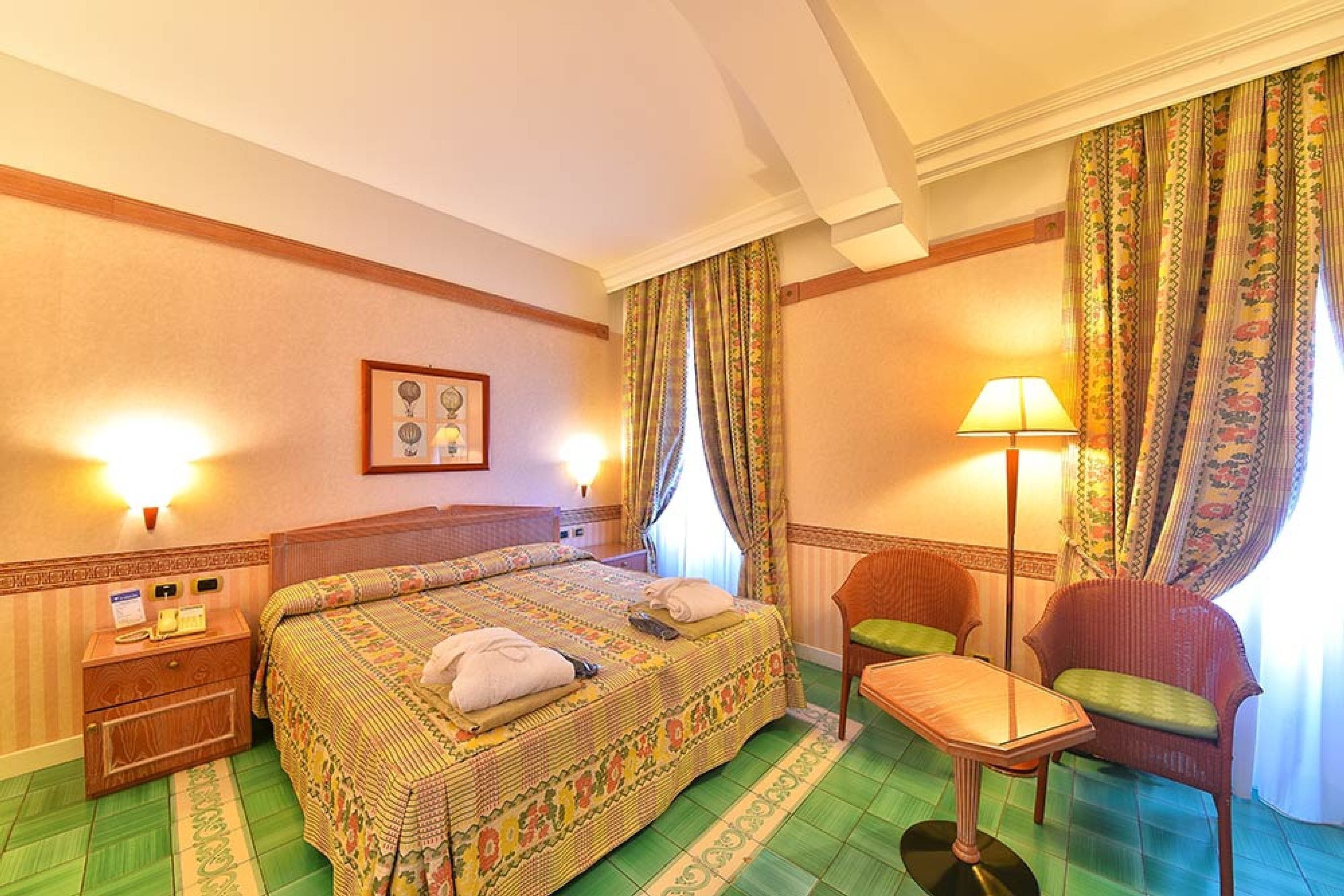 A hotel room with a bed, a chair, a table, a lamp, and a picture on the wall.