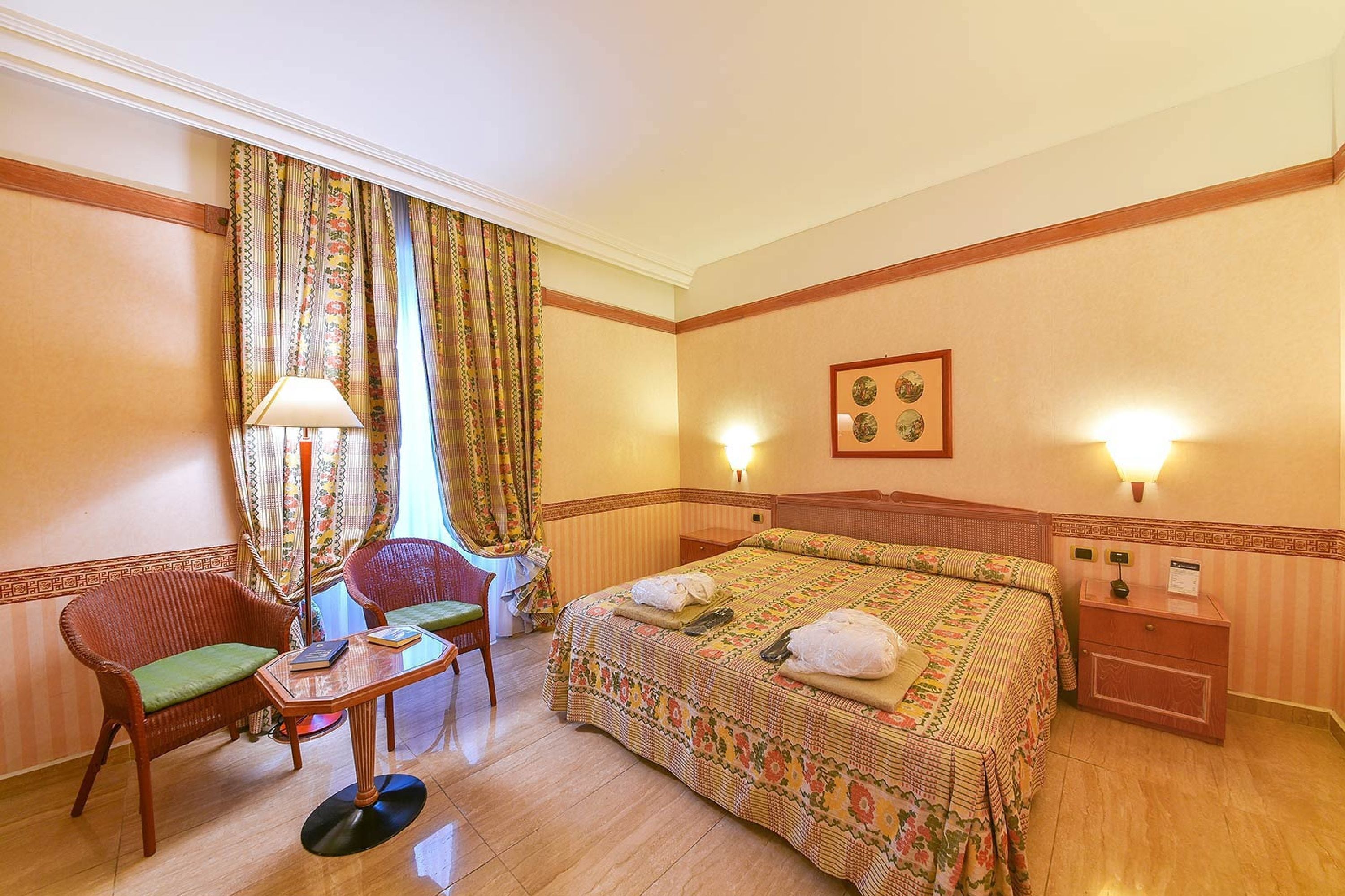 Una habitació d'hotel amb un llit, una cadira, una taula, una làmpada i una tauleta de nit.