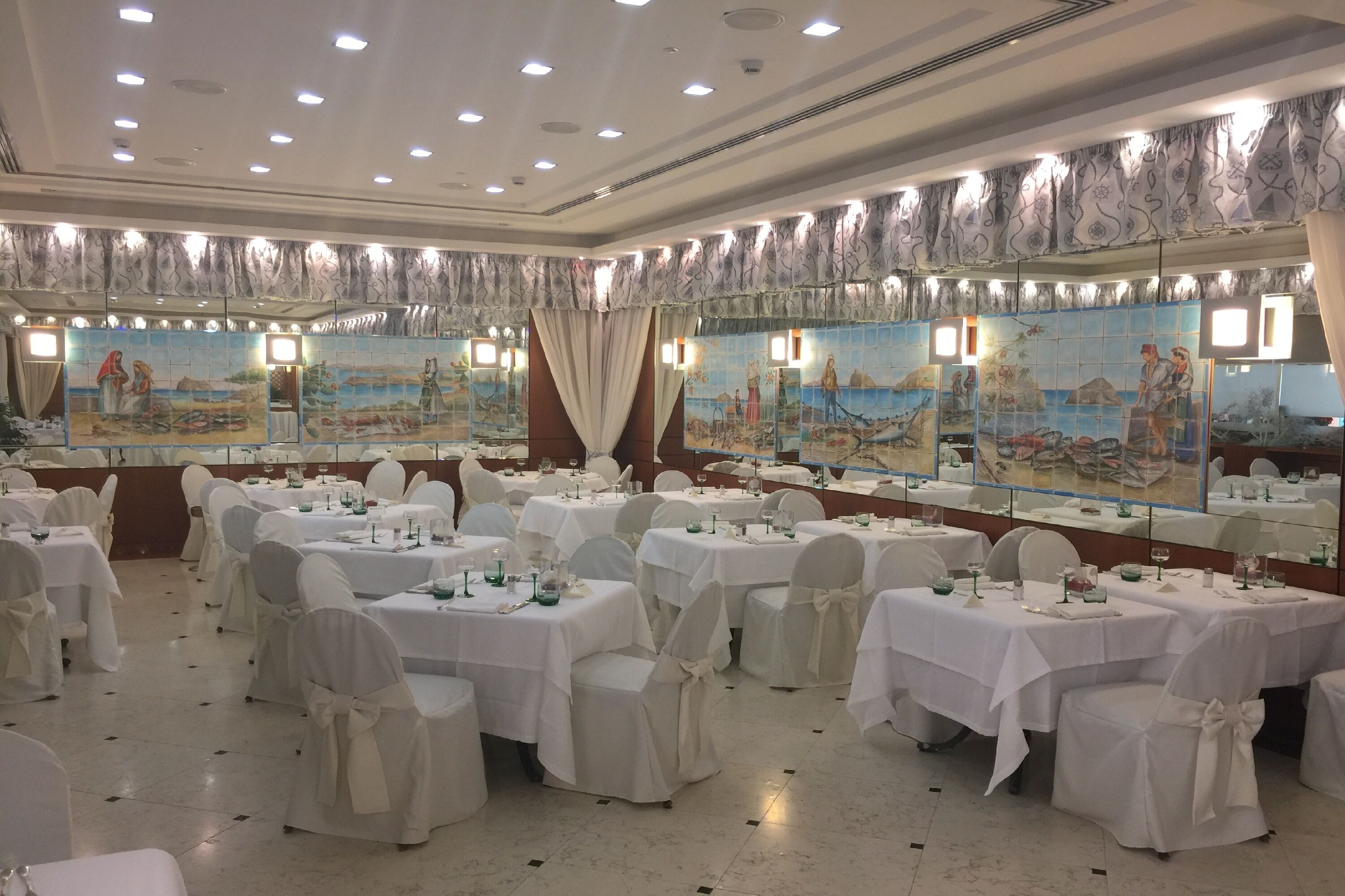 A banquet hall with round tables, white tablecloths, and chairs with white covers.