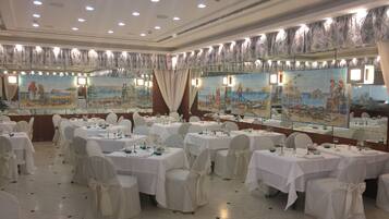 A banquet hall with round tables, white tablecloths, and chairs with white covers.