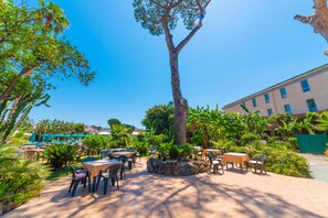 An outdoor patio area with tables and chairs, surrounded by greenery and a large tree. - Grand Hotel Delle Terme Re Ferdinando (Ischia)
