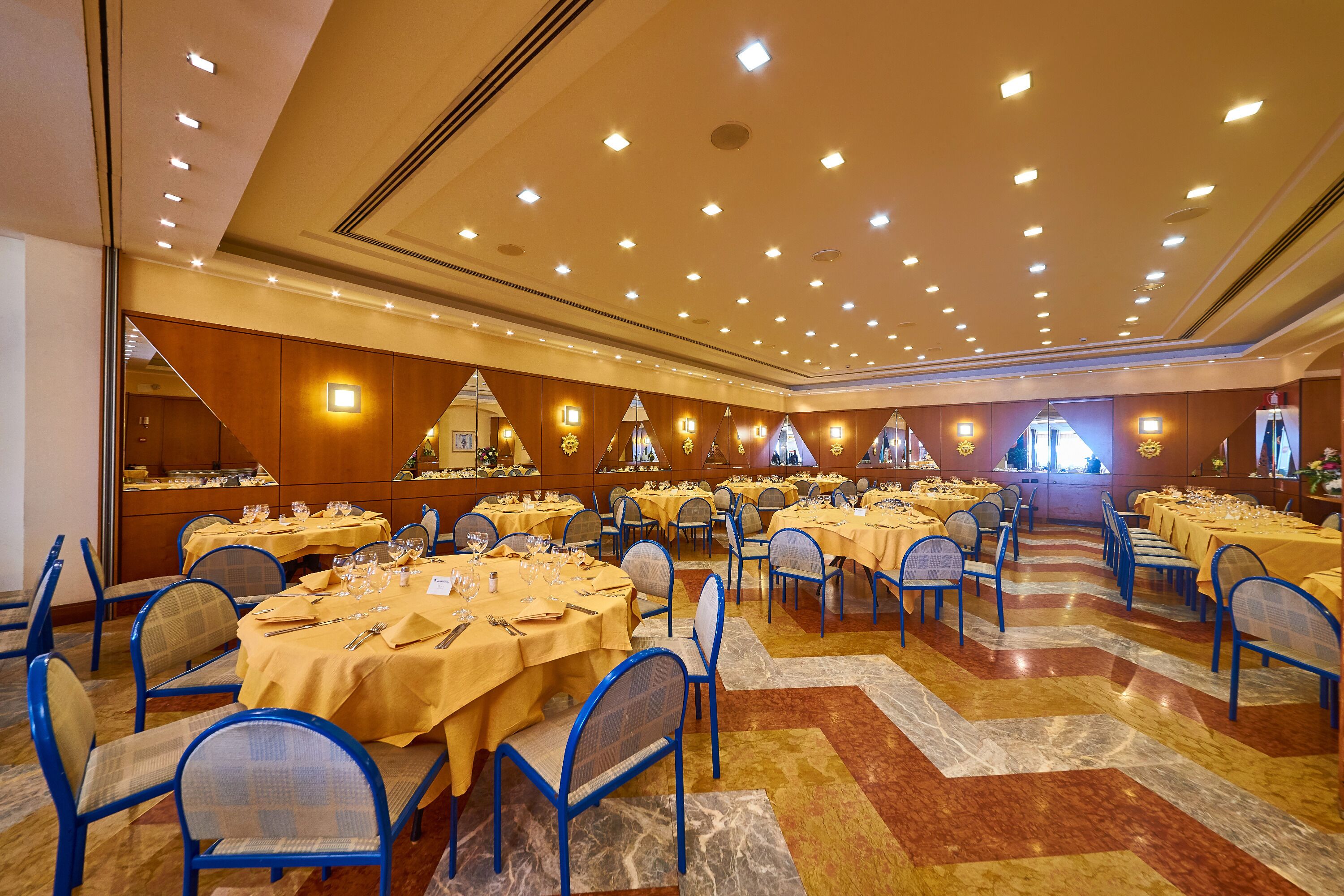 A banquet hall with multiple round tables, blue chairs, and a patterned floor.