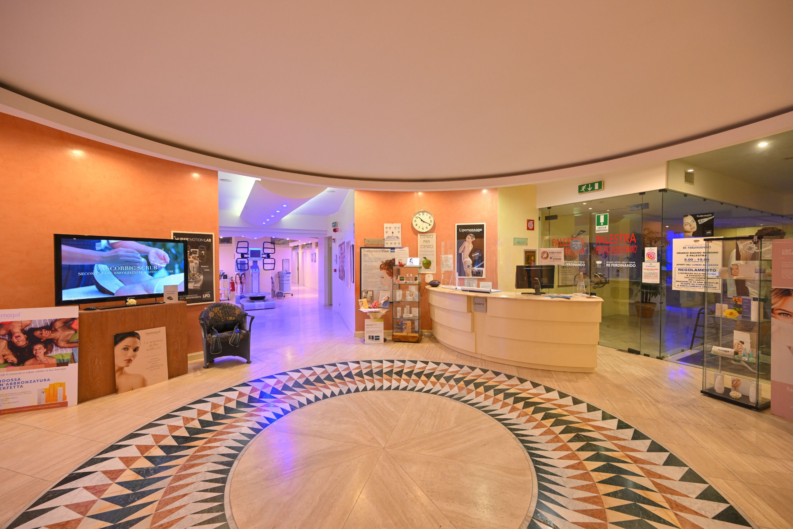 A hotel lobby with a reception desk, a clock, and a TV displaying a program.