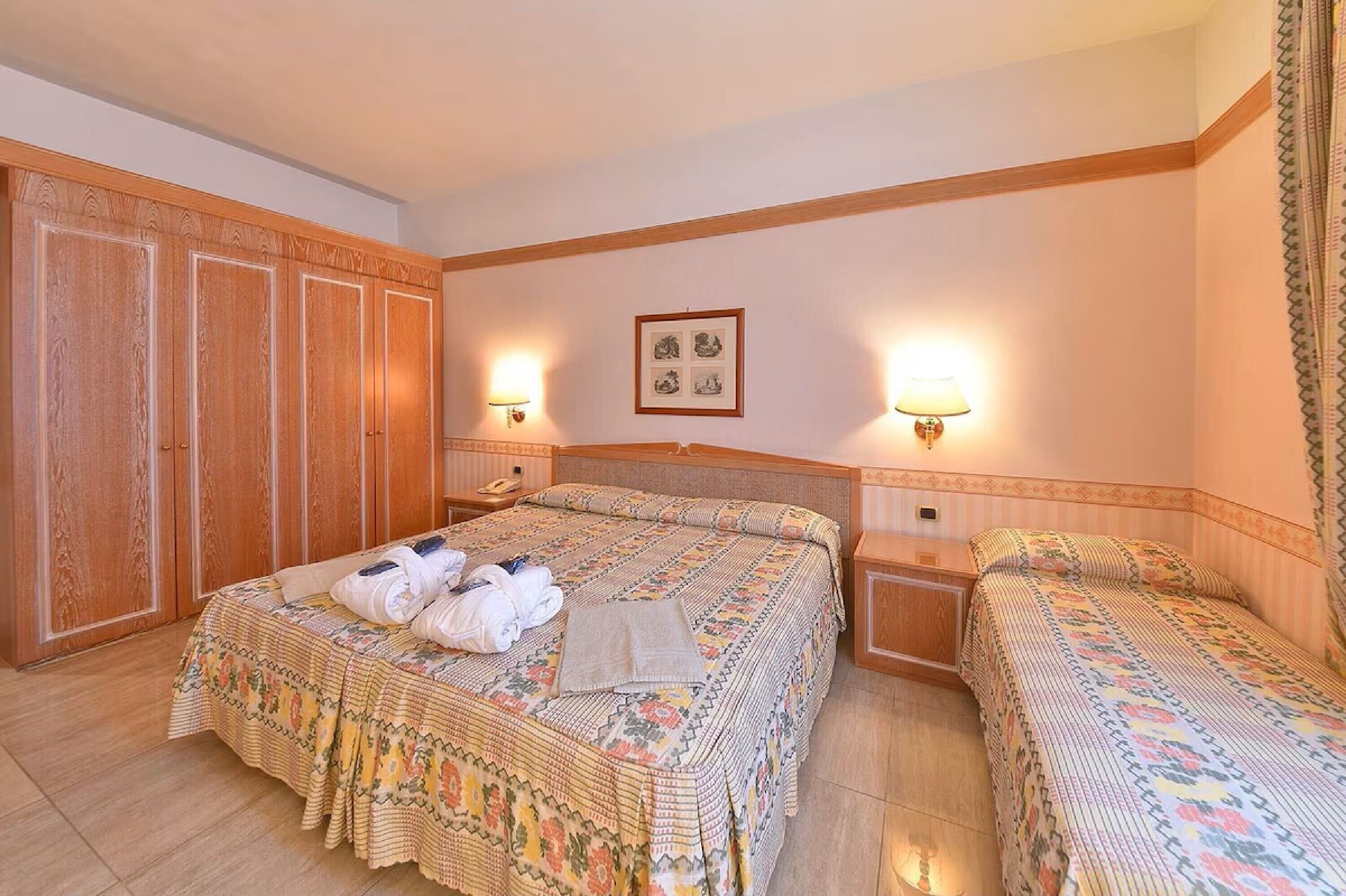A hotel room with a large bed, two bedside tables, a wardrobe, and wall-mounted lamps.