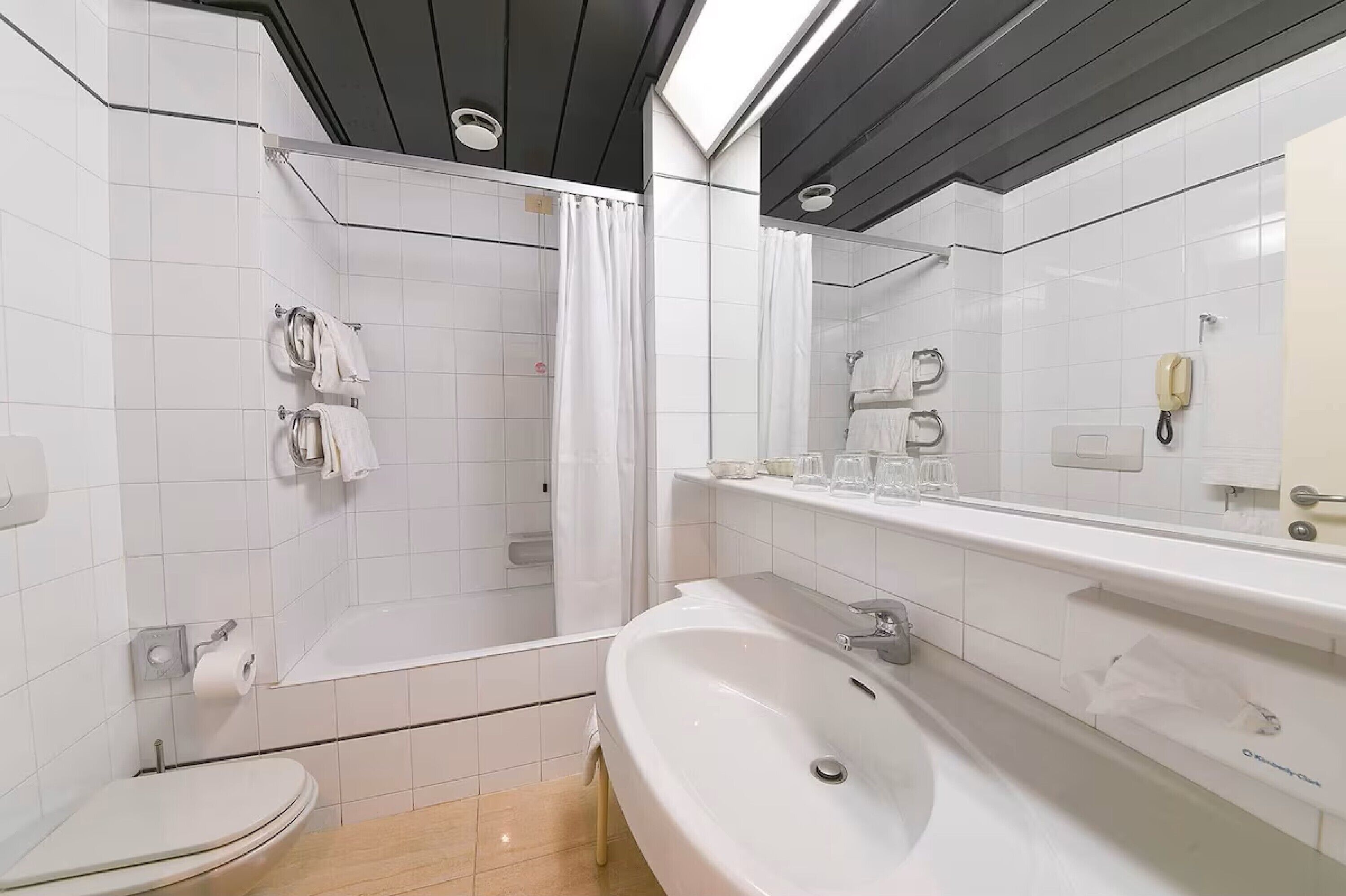 A modern bathroom with a toilet, sink, shower, and a large mirror.