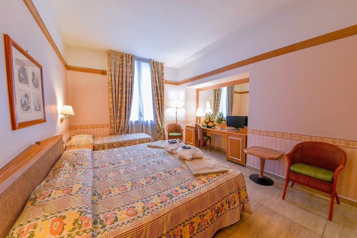 Una camera d'albergo con due letti, una scrivania con una sedia, una televisione e un piccolo tavolino.