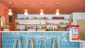 Un bar con pared de azulejos azules, taburetes de madera y estantes con botellas y vasos.