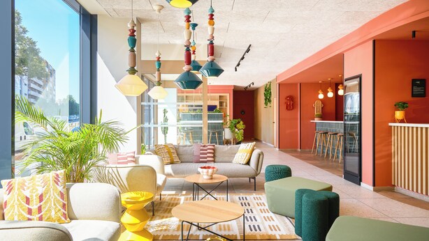 Una sala de estar moderna con un sofá, una mesa de centro y un otoman verde. Se observa una zona de cocina con una barra y taburetes.