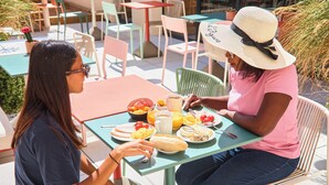 Dos personas sentadas en una mesa al aire libre con comida, rodeadas de sillas y mesas.