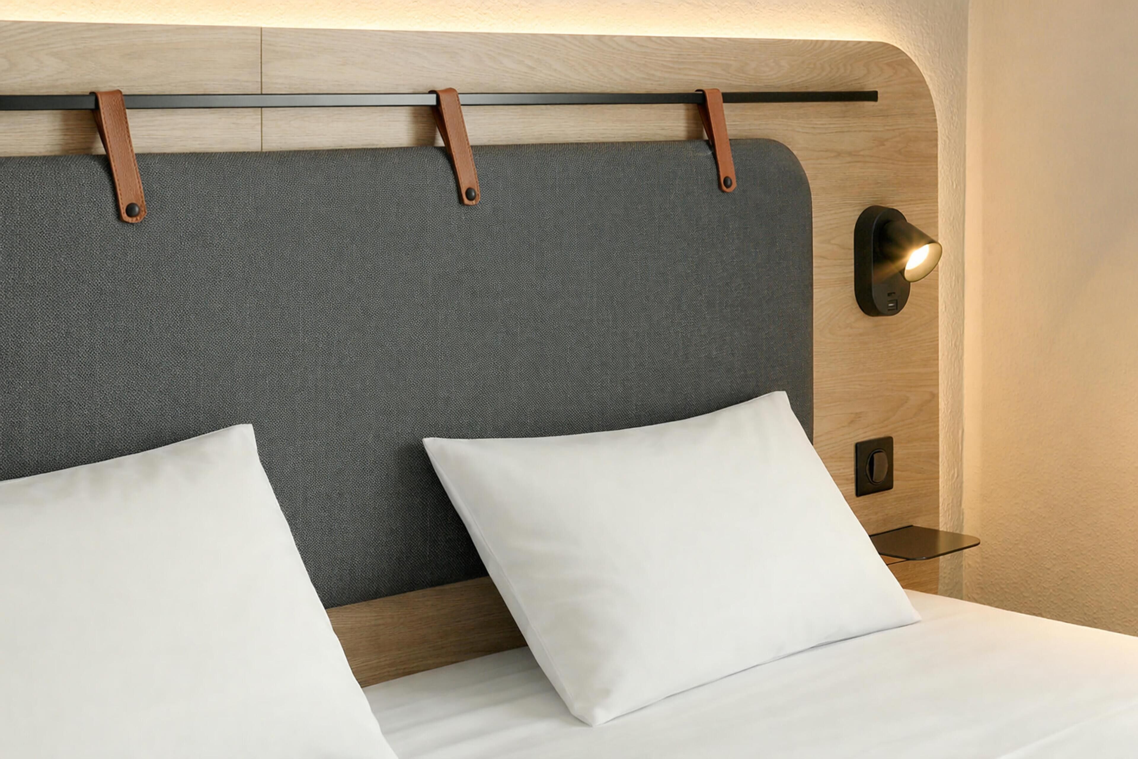 A bed with a grey headboard, two white pillows, and a bedside table with a lamp.