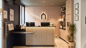 A reception desk with a modern design, featuring a wooden panel and a lit-up logo above it. - Campanile PRIME - Paris 15 Tour Eiffel (Paris)