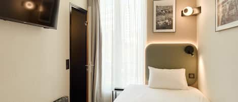 Habitación de hotel con cama, televisor montado en la pared, un cuadro enmarcado y una ventana con cortinas.