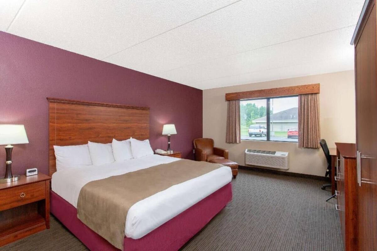 Een hotelkamer met een groot bed, een bureau, een stoel, een raam met uitzicht en een airconditioner.