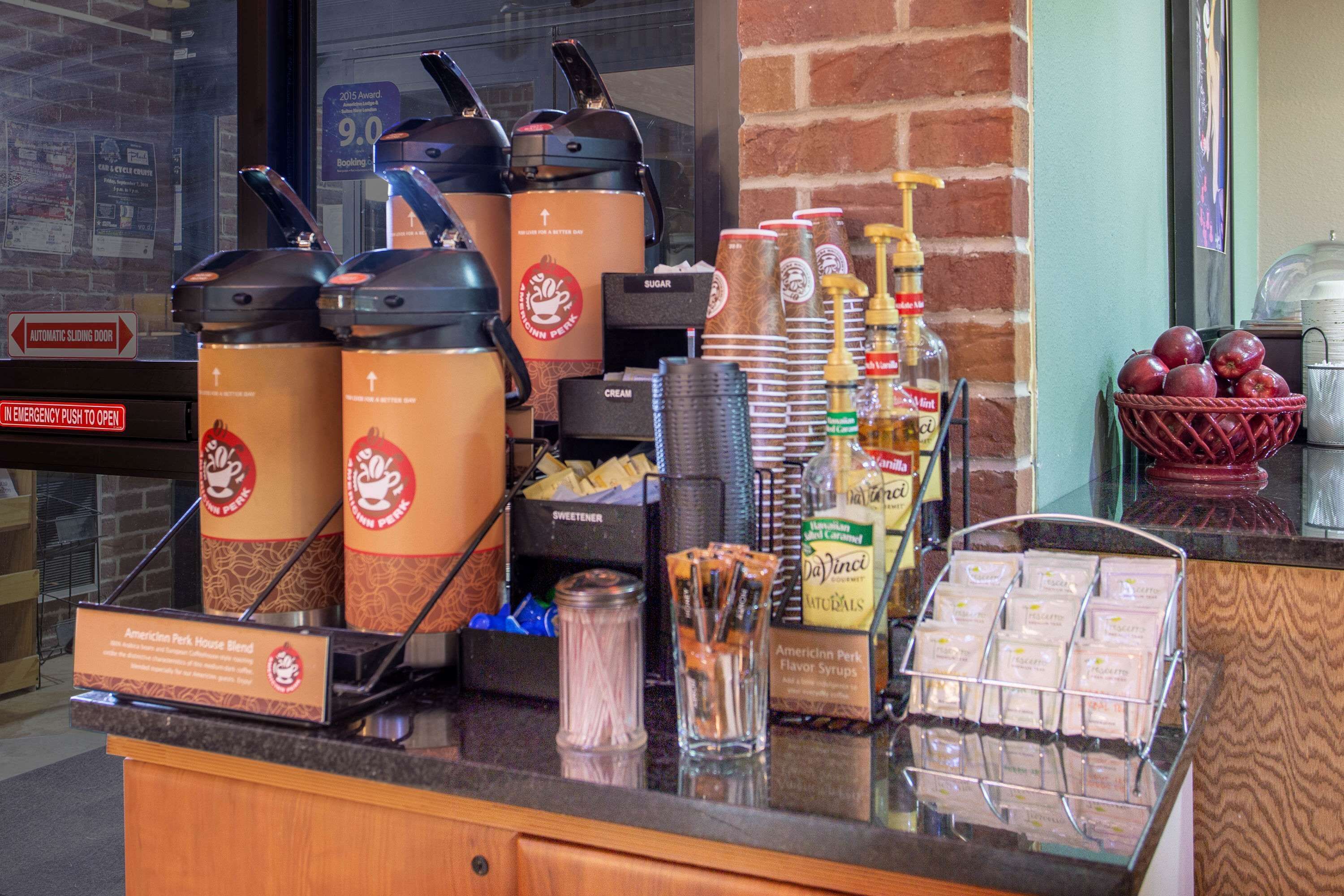 Una estación de café con varias máquinas de café, azúcar, crema y jarabes.