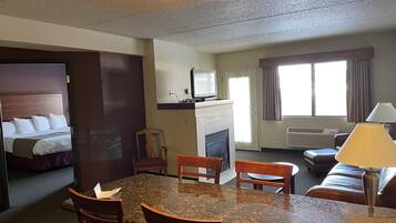A hotel room with a bed, a dining table with chairs, a fireplace, a television, and a window with curtains.