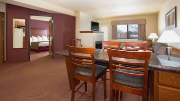 A hotel room with a dining area, a bed, a television, and a fireplace.